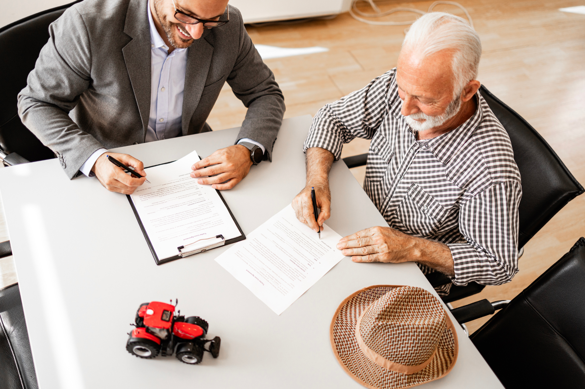 Photo of an Investment Advisor sitting with an elderly man, signing papers and smiling.